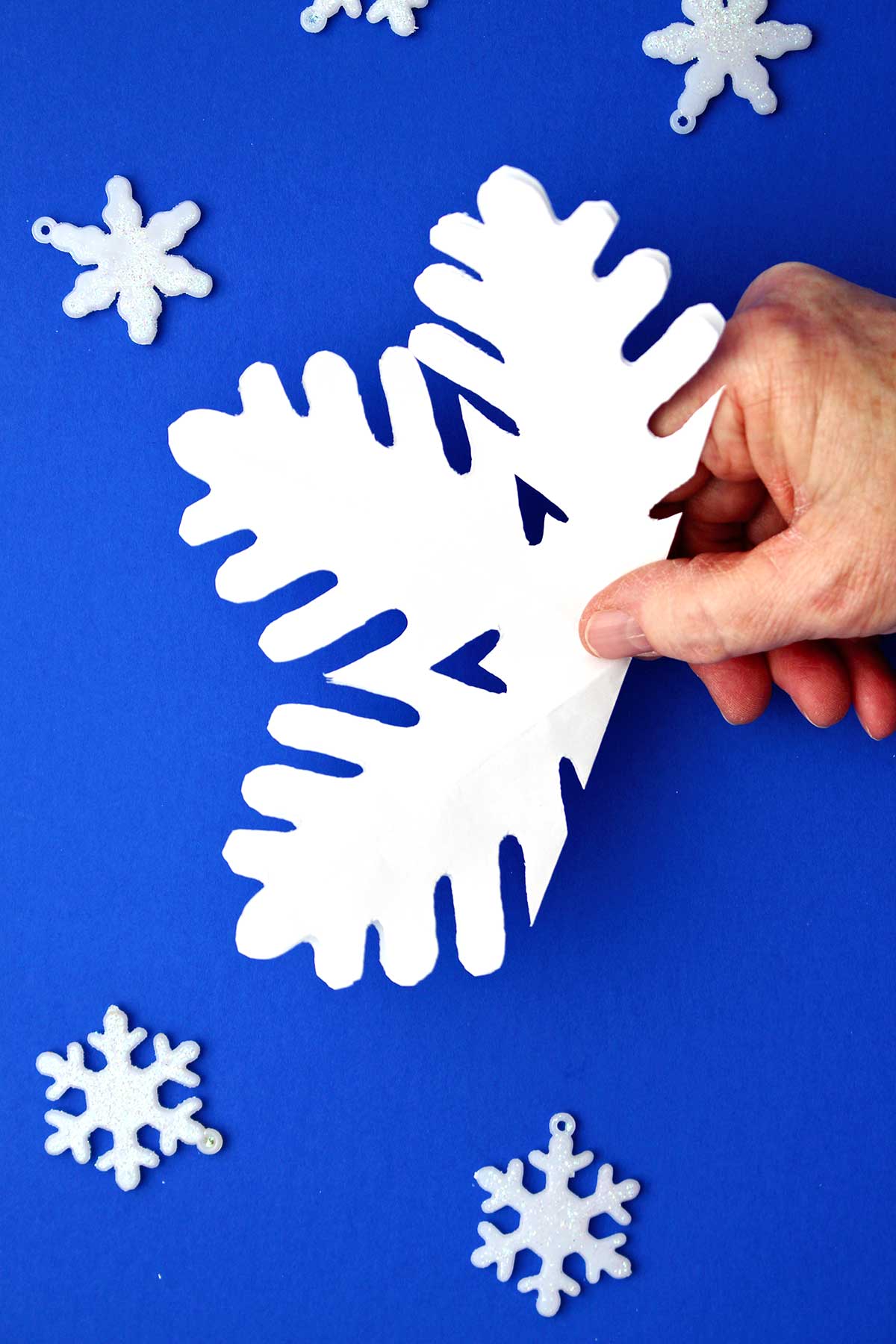 Hand holding half unfolded snowflake made from white paper.