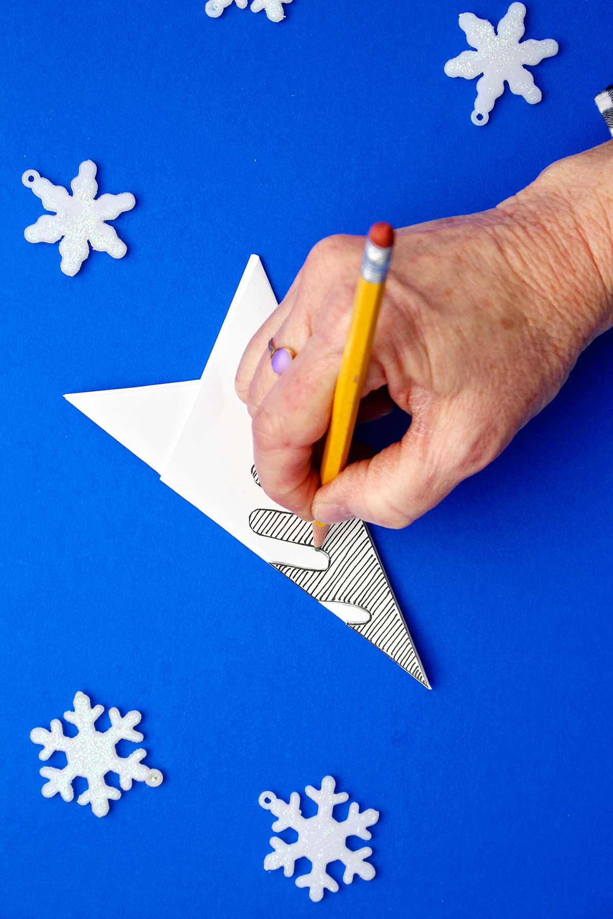 Hand tracing snowflake template on folded piece of white paper.