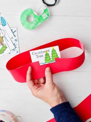 Hand coloring in printable of Christmas cards for headband game and hand holding finished headband with "Christmas Tree" card in it.
