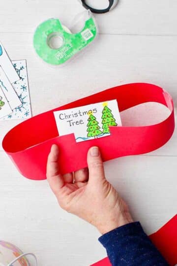 Hand coloring in printable of Christmas cards for headband game and hand holding finished headband with "Christmas Tree" card in it.