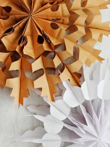 Two completed paper bag snowflake. One in brown and one in white.