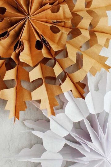 Two completed paper bag snowflake. One in brown and one in white.