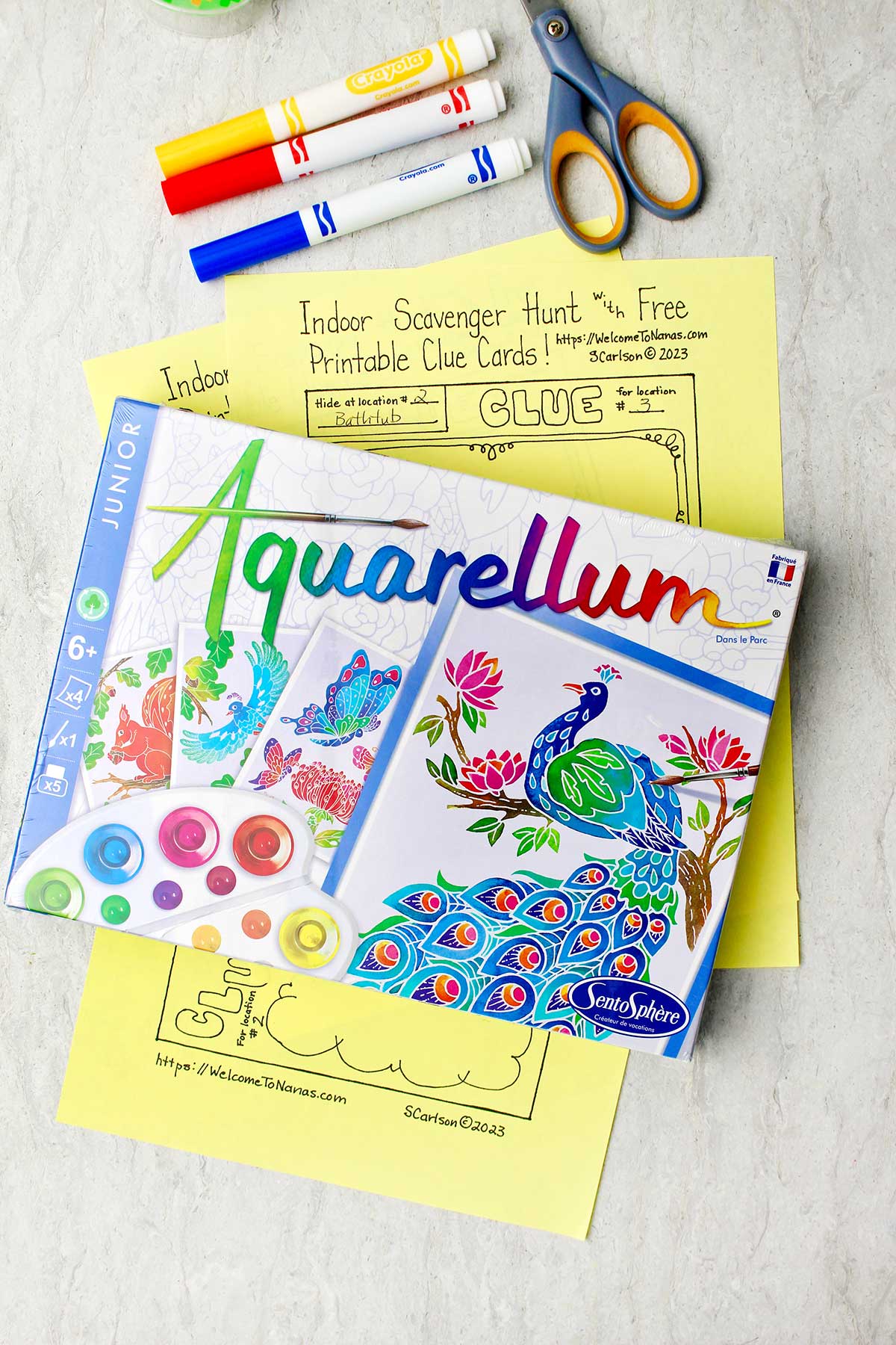 Aquarellum craft kit resting on stacks of clue card papers and markers and scissors near by.