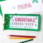 A final DIY Christmas Coupon Book sitting near an envelope addressed to "papa", with colored pencils nearby.