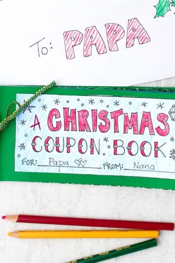 A final DIY Christmas Coupon Book sitting near an envelope addressed to "papa", with colored pencils nearby.