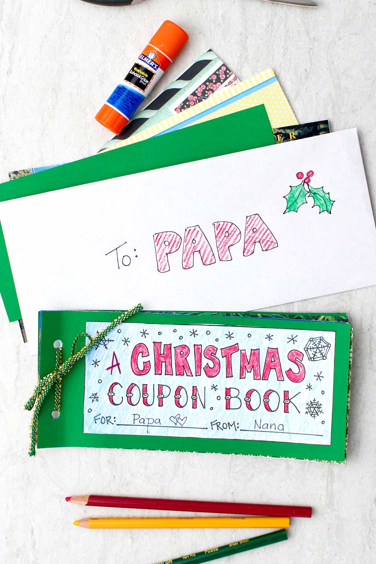 A final DIY Christmas Coupon Book sitting near an envelope addressed to "papa", with colored pencils nearby.