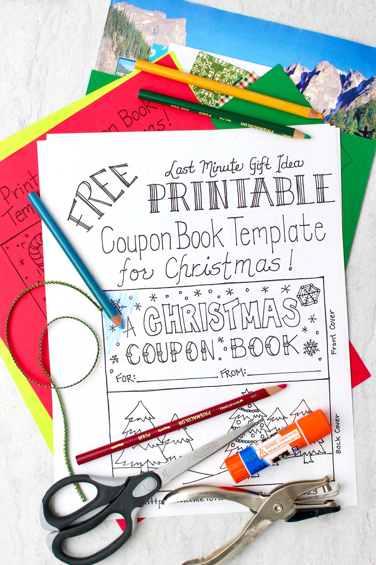 A free printable coupon book template sitting on a stack of colorful papers, scissors, a hole punch, glue, and colored pencils nearby.