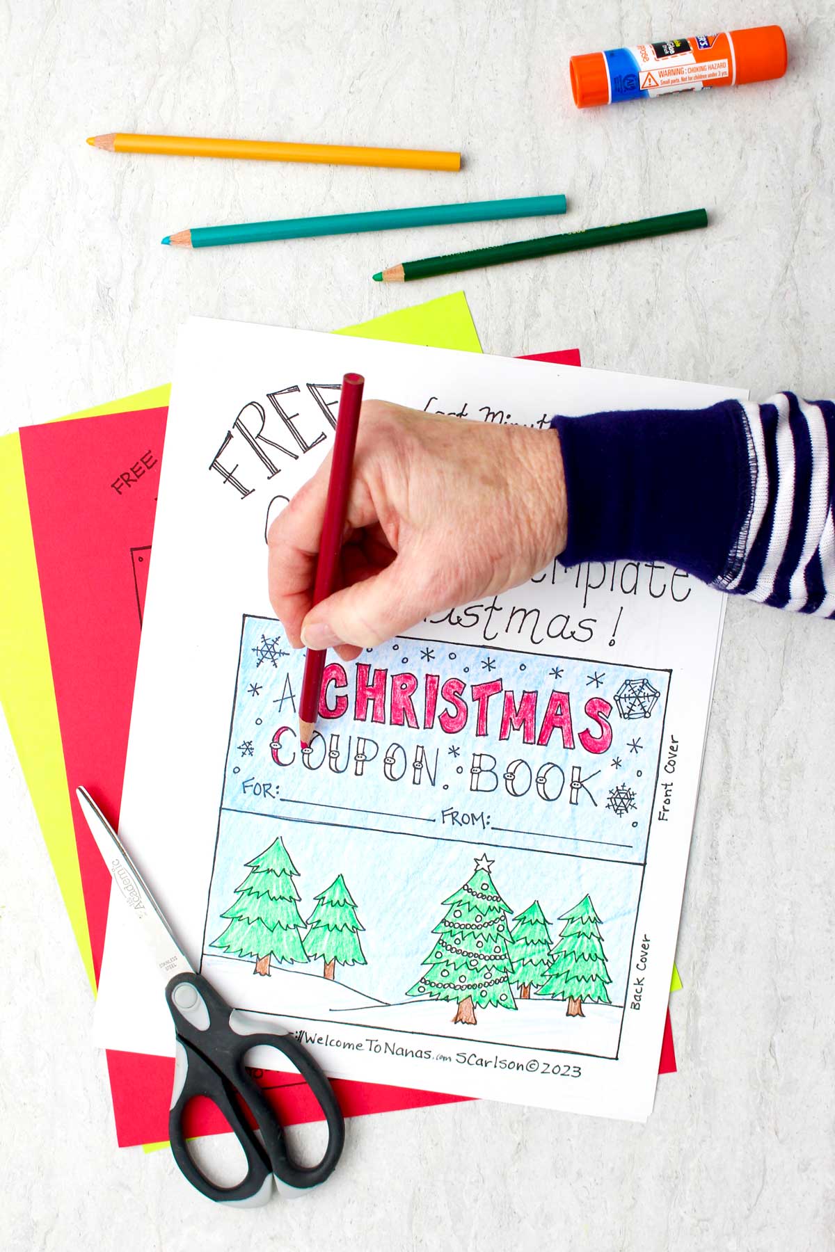 Someone coloring a printed Christmas coupon book template with a red colored pencil.