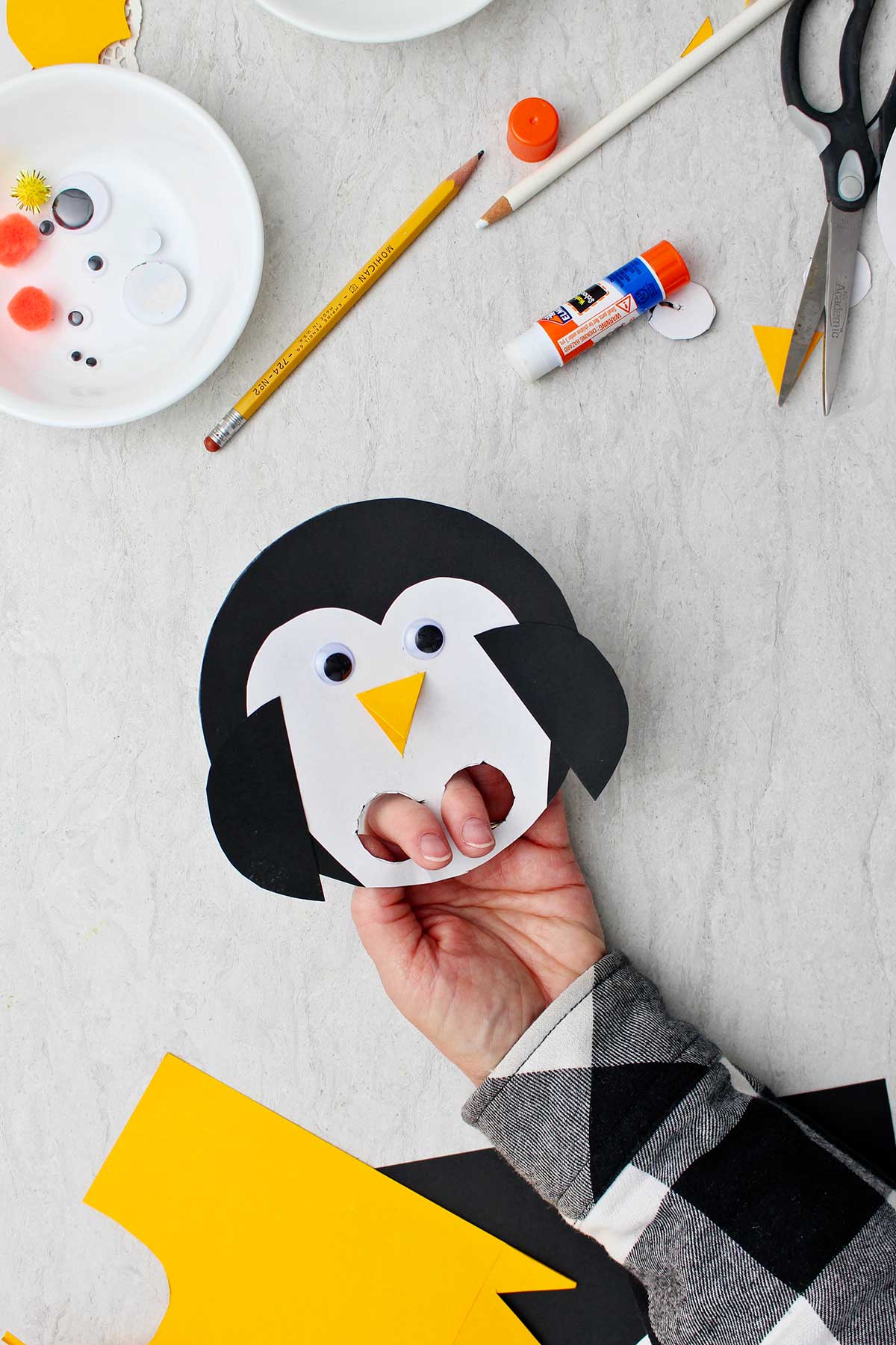 Hand holding completed Paper Penguin Craft with holes cut out for fingers.