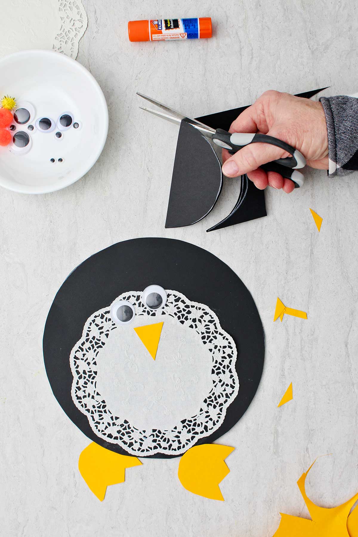 Hand cutting a piece of black paper for the doily Paper Penguin Craft with supplies near by.