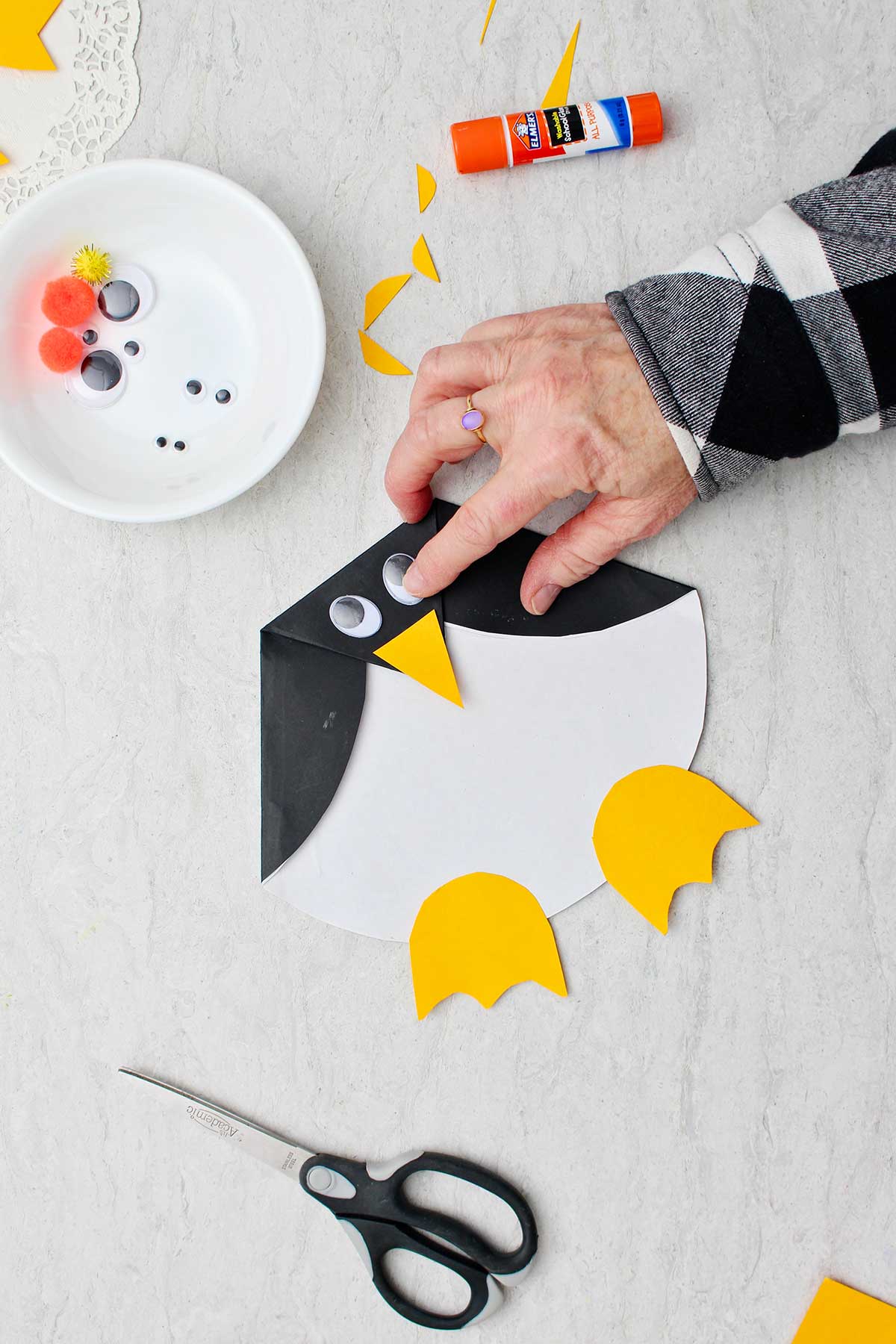 Hand gluing on googly eye for the folded Paper Penguin Craft.