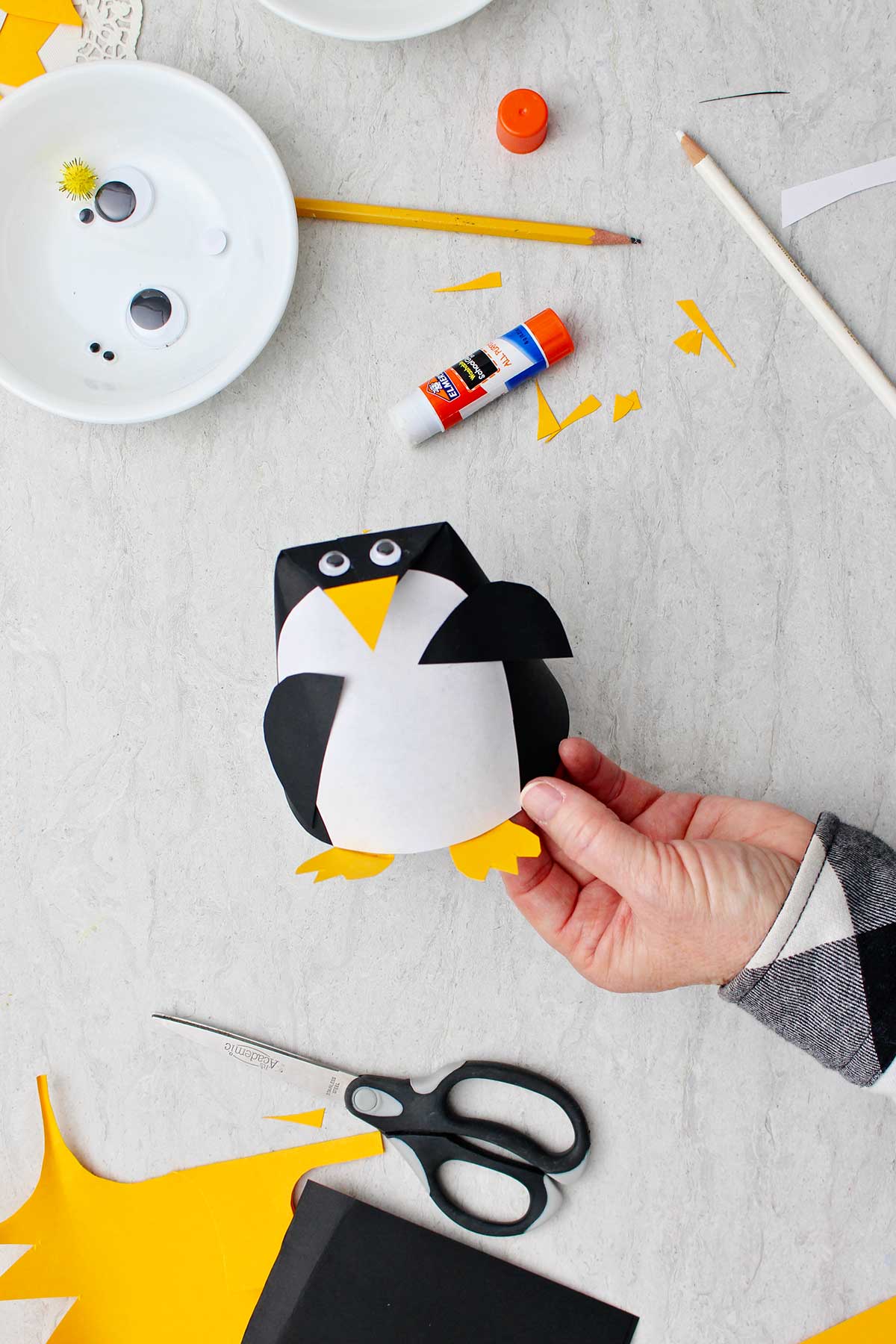 Completed cone shaped Paper Penguin Craft with supplies near by.