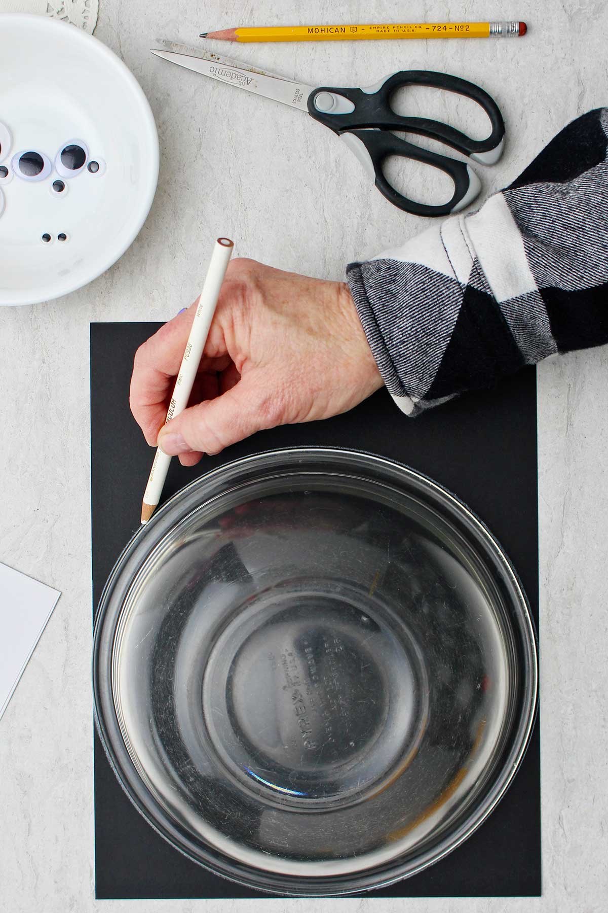 Hand tracing black piece of paper with bowl.
