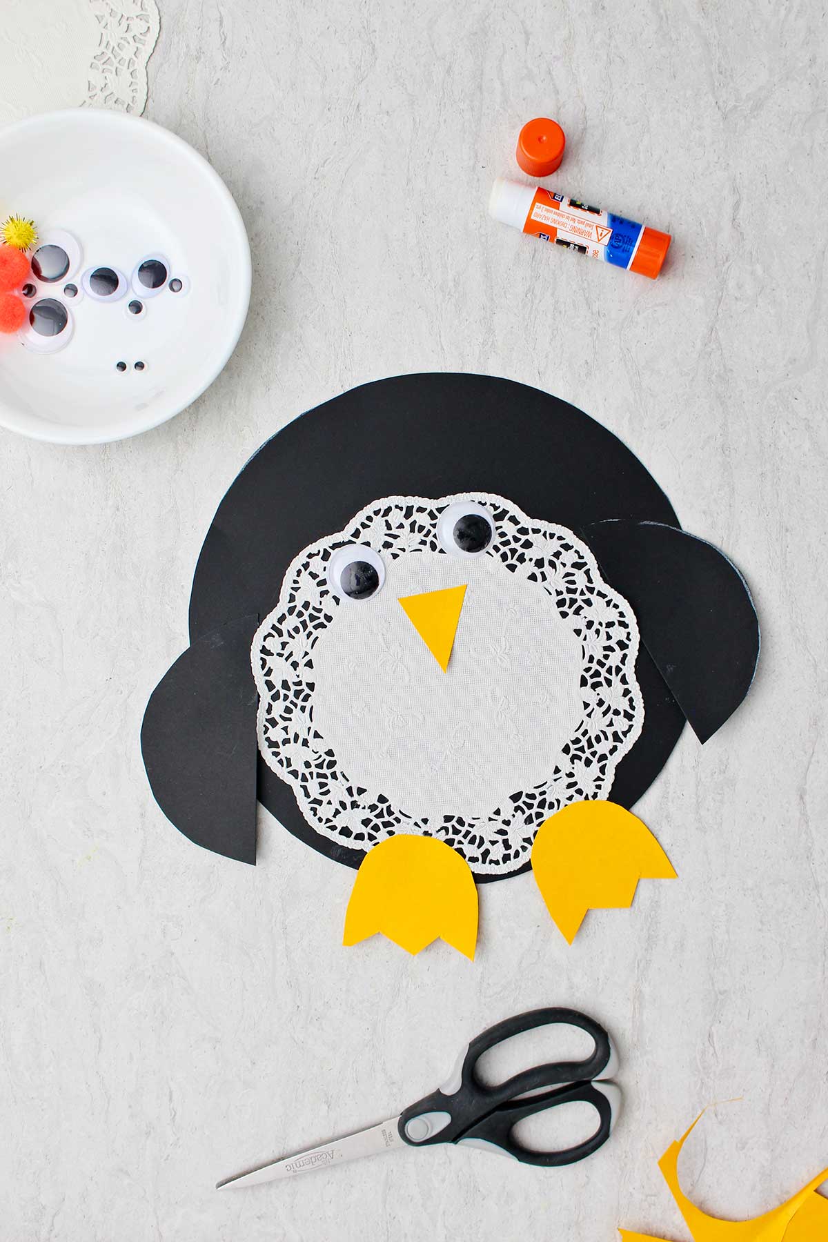 Completed doily Paper Penguin Craft with supplies near by.