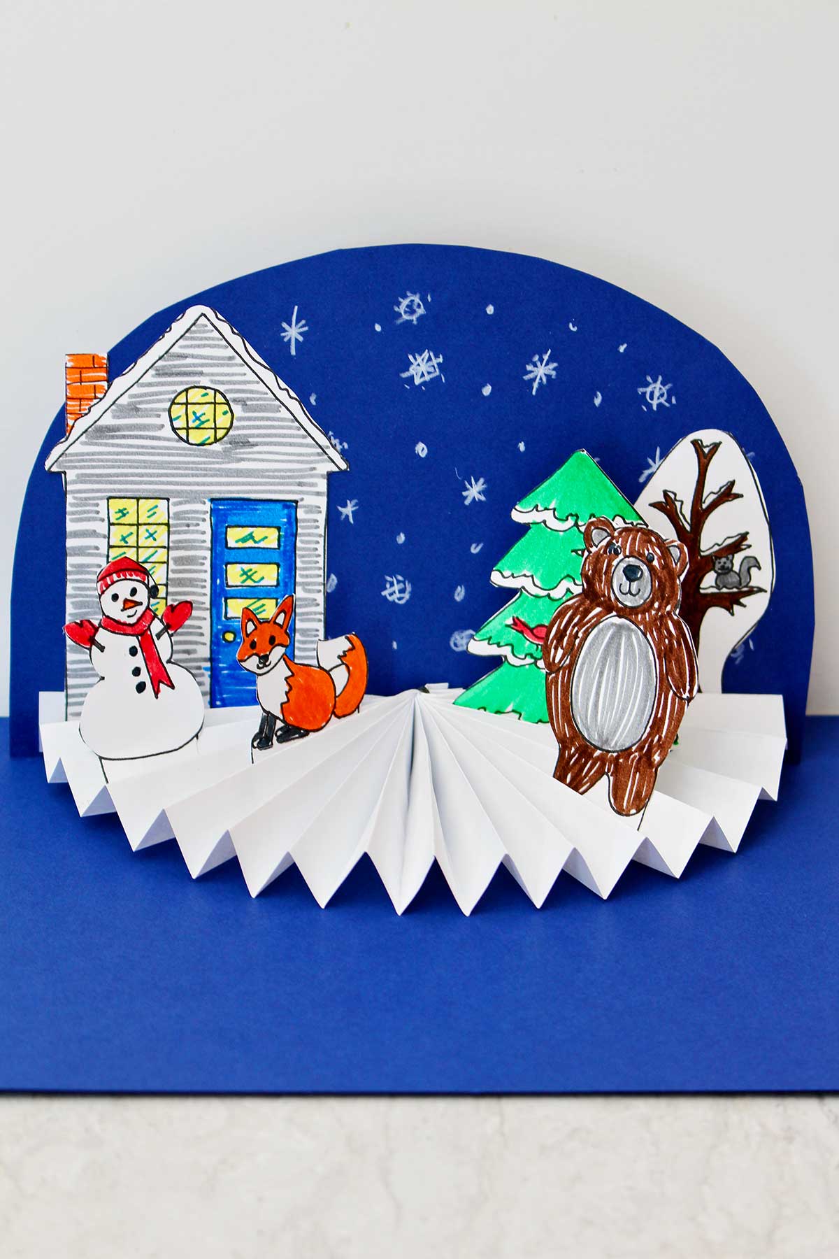 Completed Easy Paper Fan Craft in a winter theme with a snowman, fox, bear and snowy blue background.