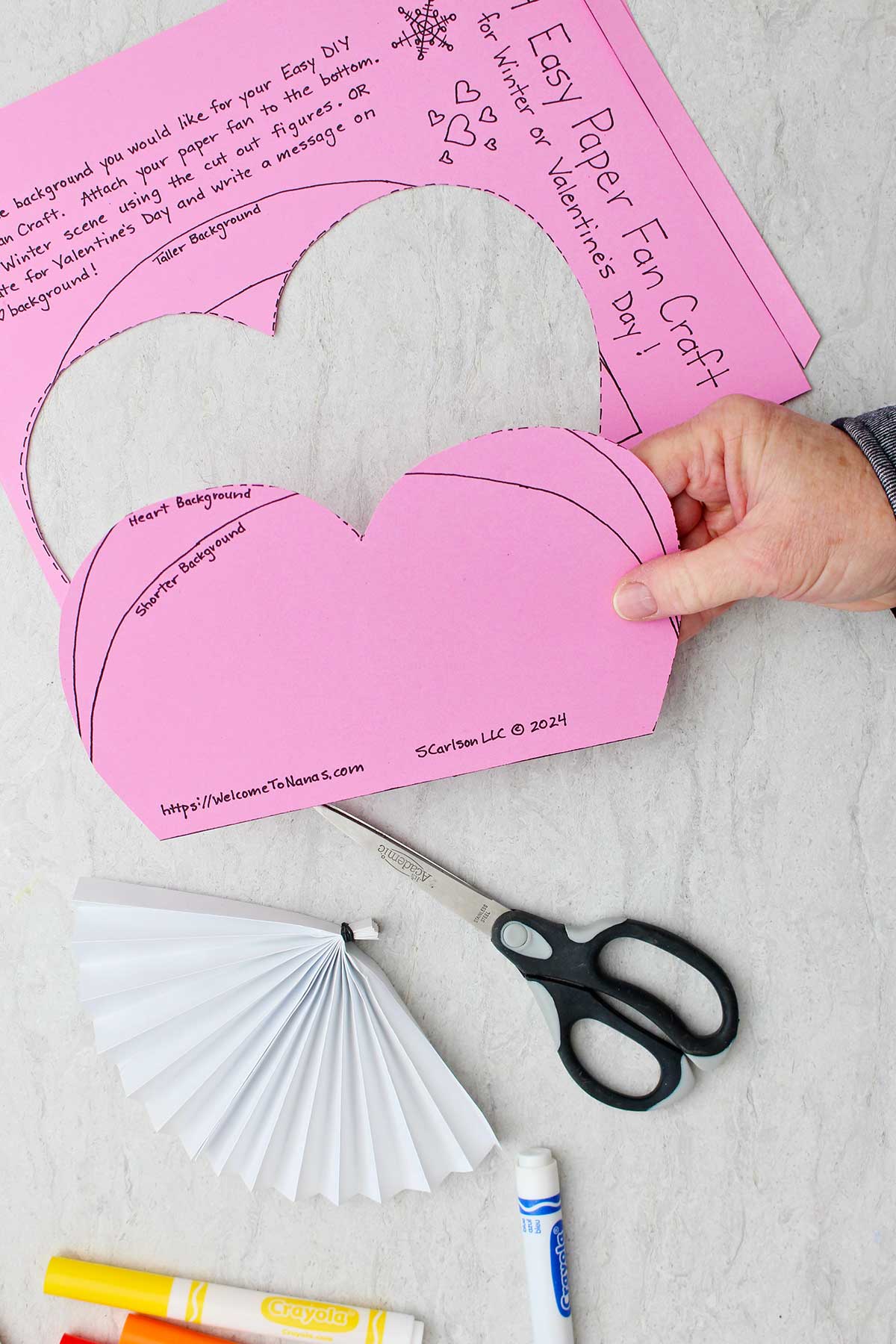 Hand holding pink heart cut out from printed template.