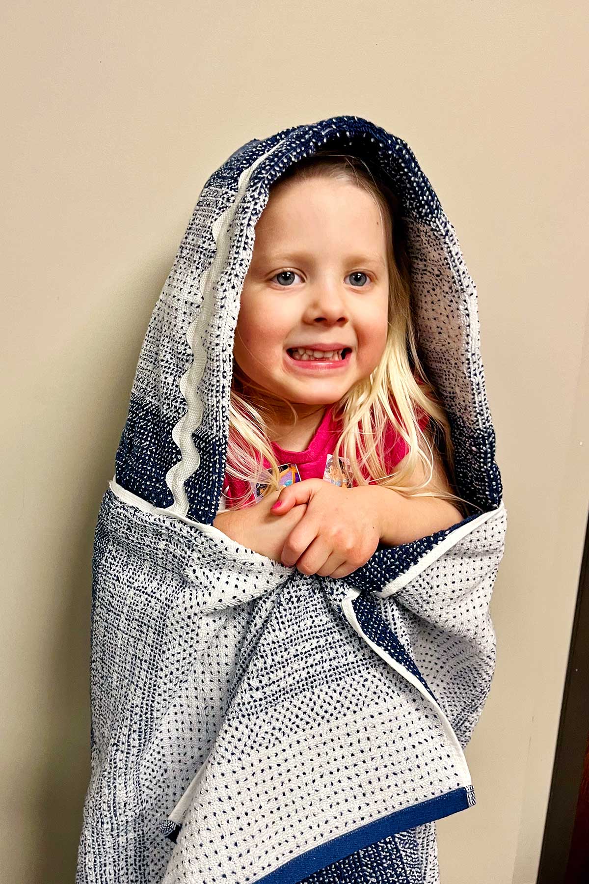 Young girl with blonde hair snuggled up in a hooded blue and white towel smiling.