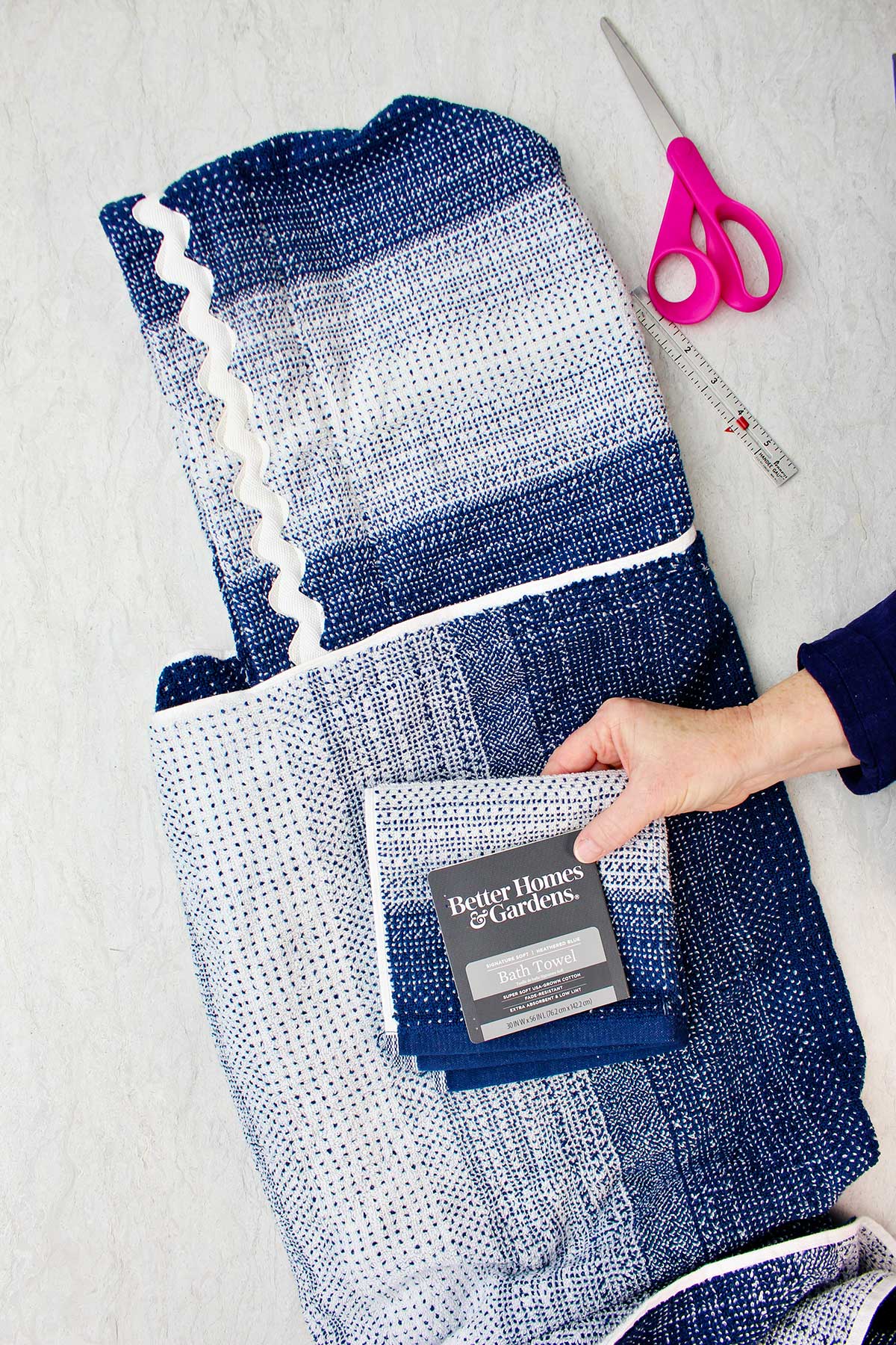 Hand holding a folded blue and white bath towel from Better Homes & Gardens with completed hooded towel in background.