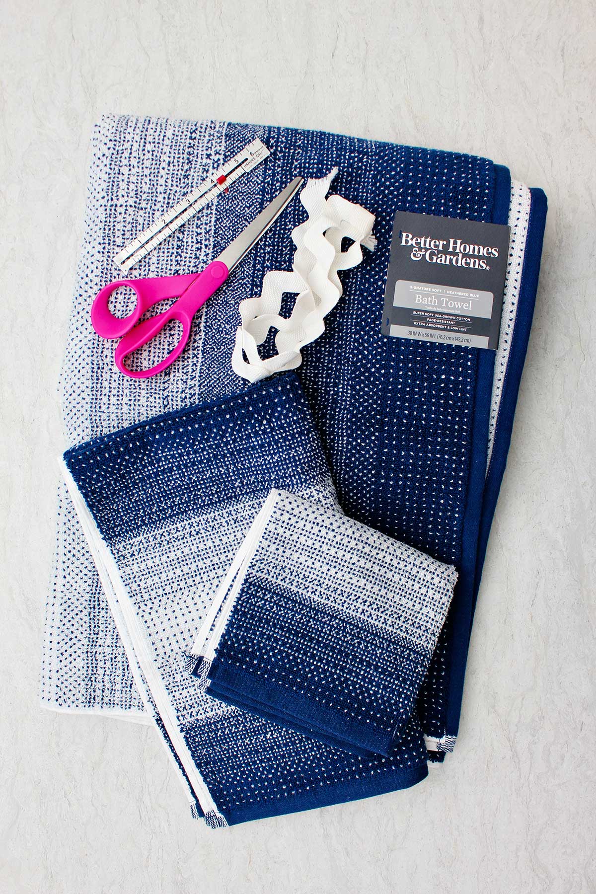 Blue and white patterned towels, a pair of pink scissors, ruler and white ric rack trim.