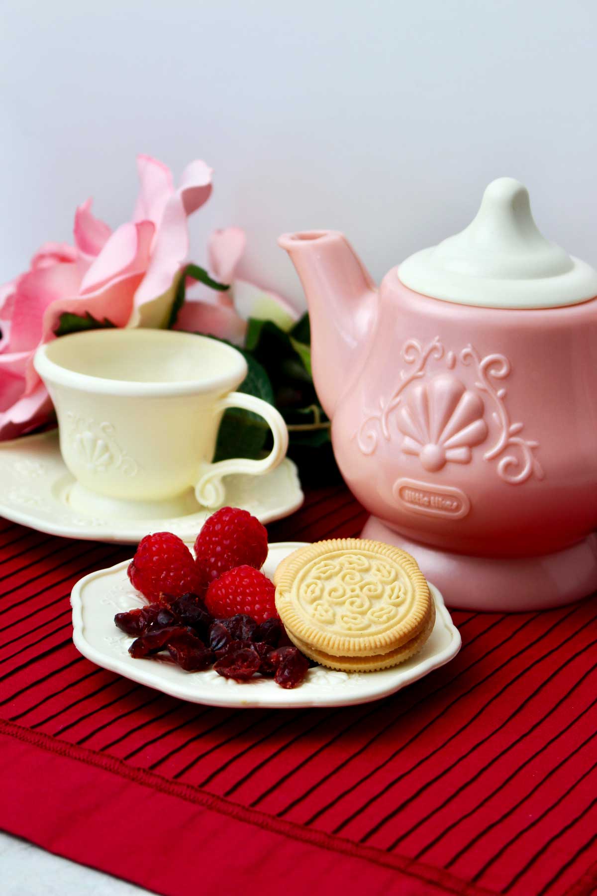 A pink and white tea set with flowers, cookies, berries and treats.