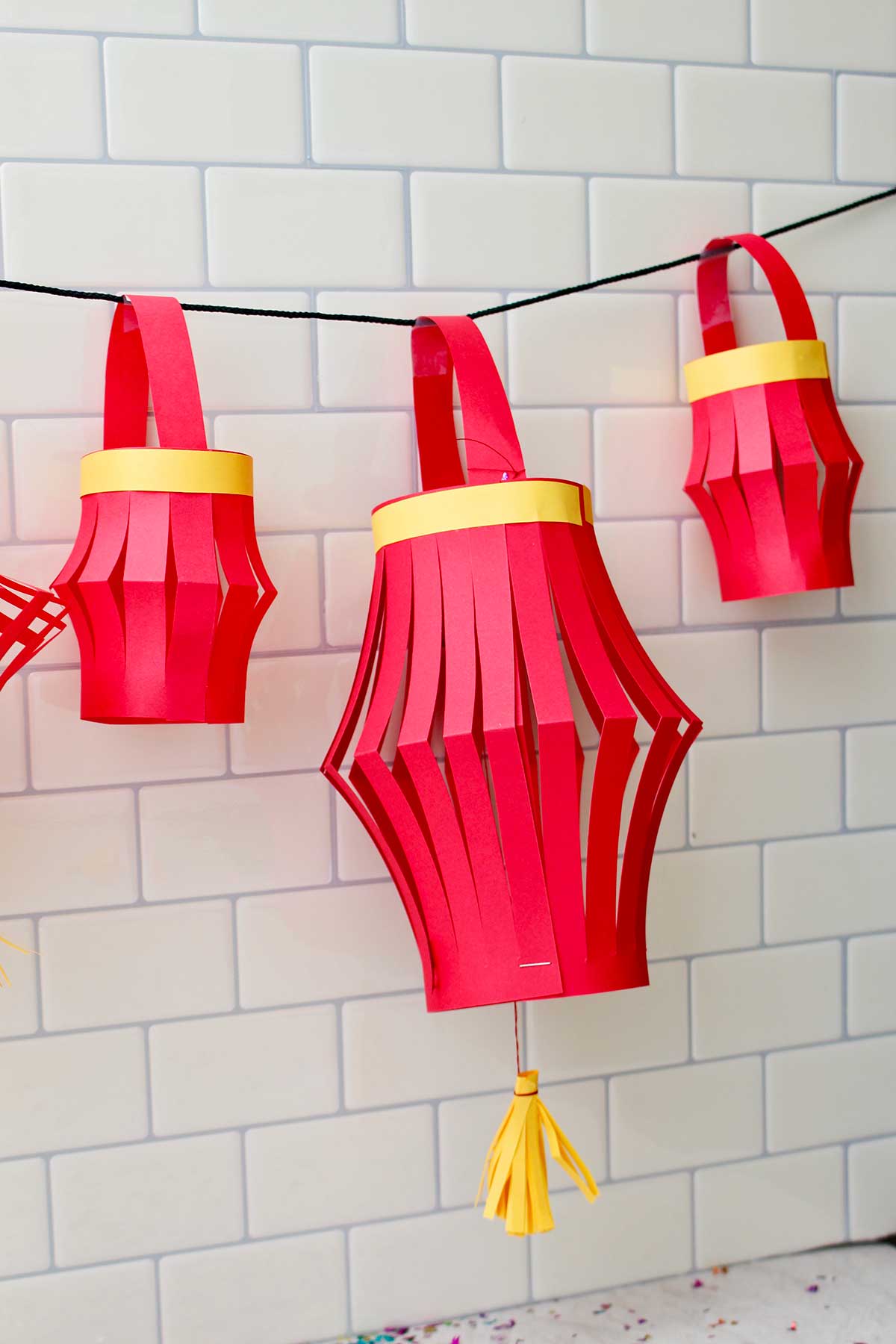Three completed paper lanterns hanging against a subway tile backdrop.