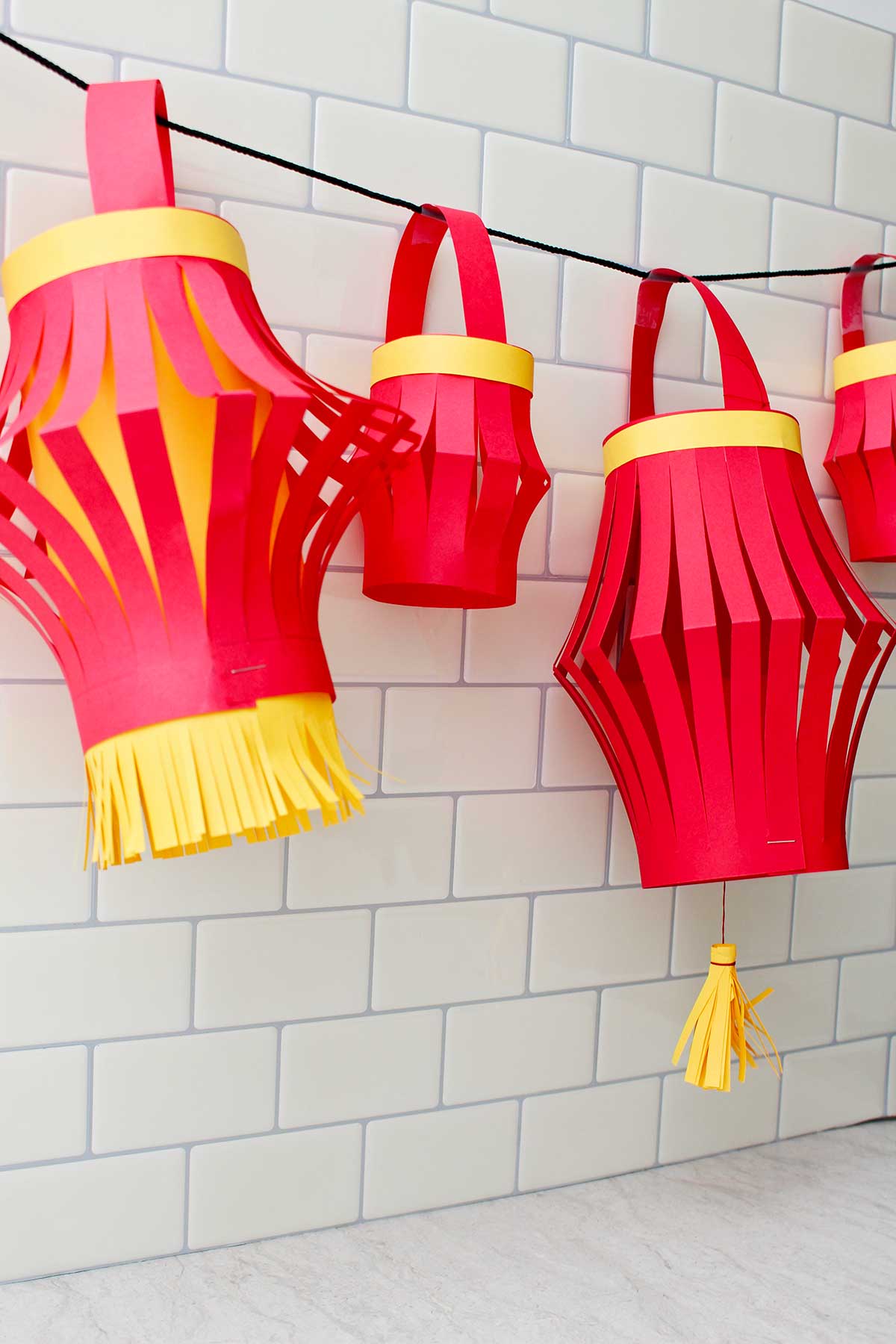 Four completed paper lanterns hanging against a subway tile backdrop.
