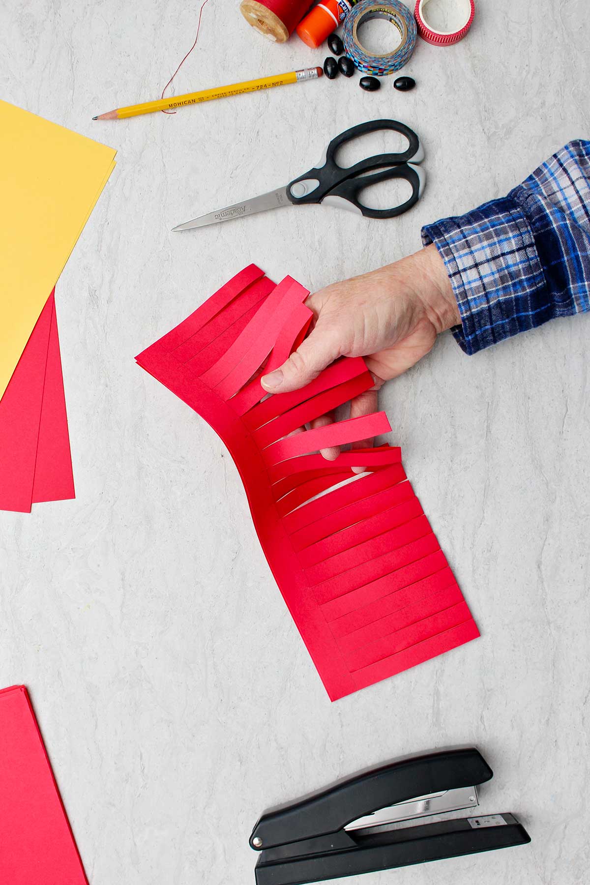 Hand showing folded piece of red paper with partially cut strips to make lantern base.