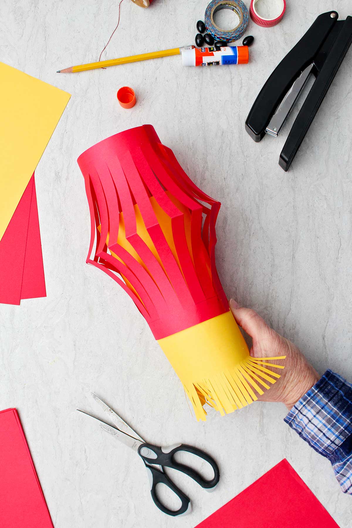 Hand placing the yellow inside part with fringe into the red paper lantern.