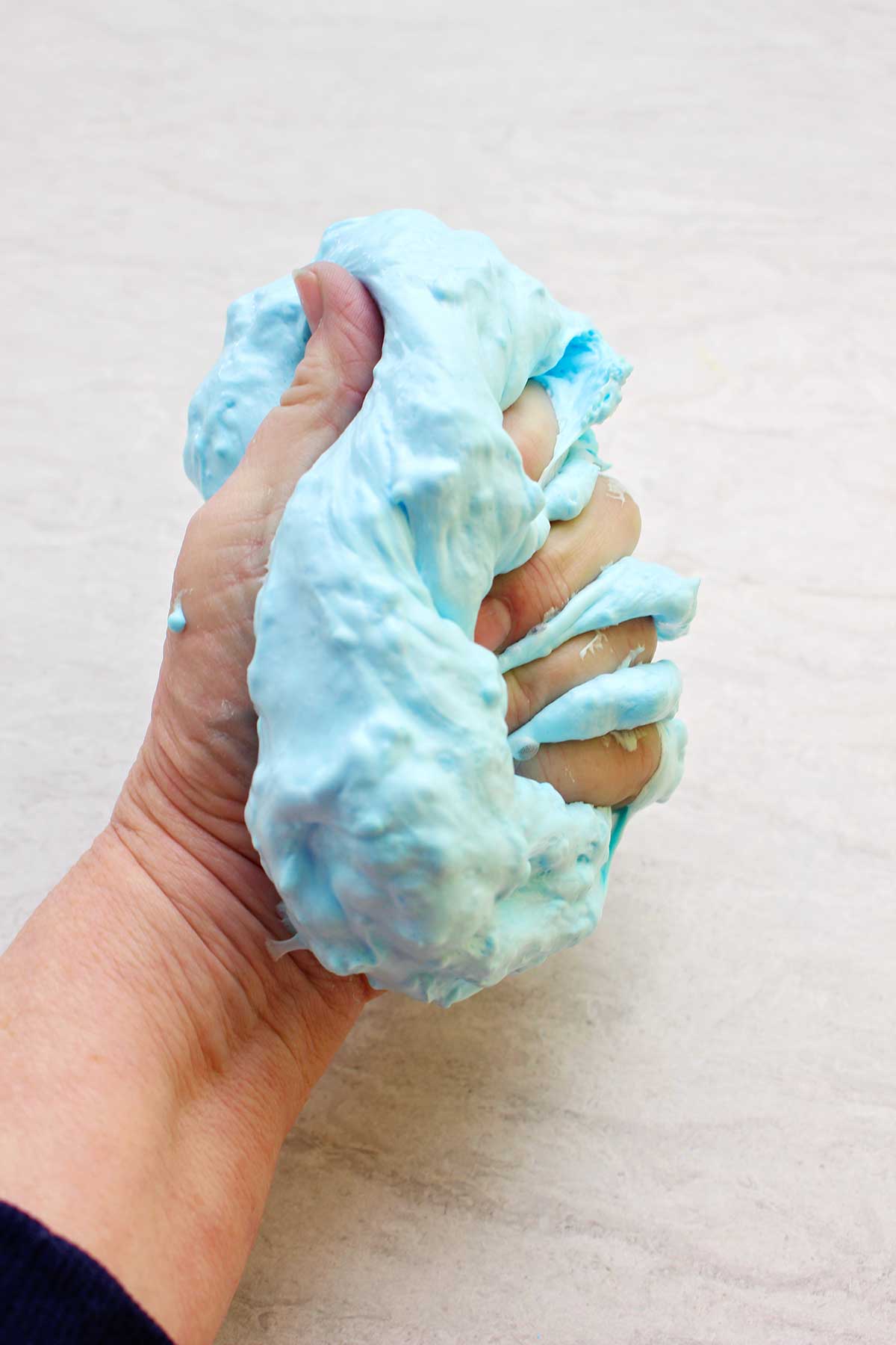 Hand squeezing the a completed batch of light blue fluffy slime.