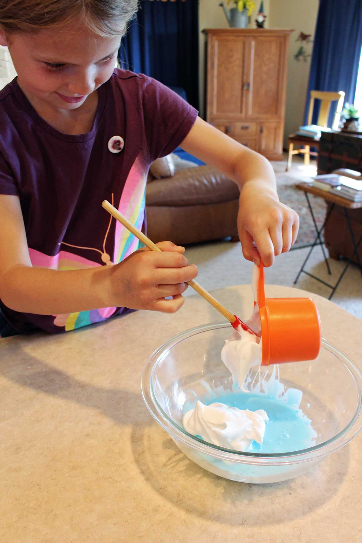 Young girl in maroon butterfly shirt adds shaving cream to a batch of fluffy slime.