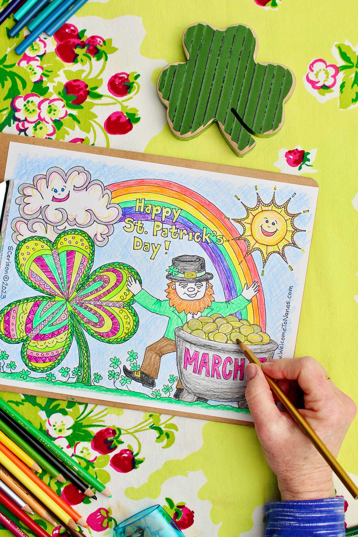Hand putting finishing touches on pot of gold on St. Patrick's Day coloring page.