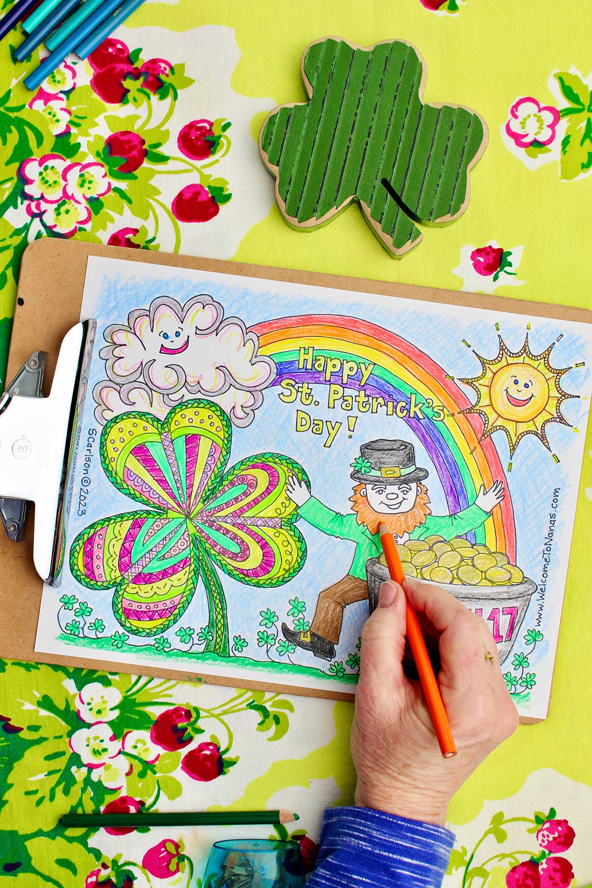 Hand putting finishing touches on leprechaun's orange beard in St. Patrick's coloring page.