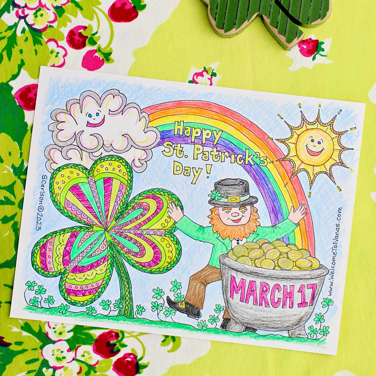 Completed St. Patrick's Day coloring page sitting on a green table cloth with strawberries on it.