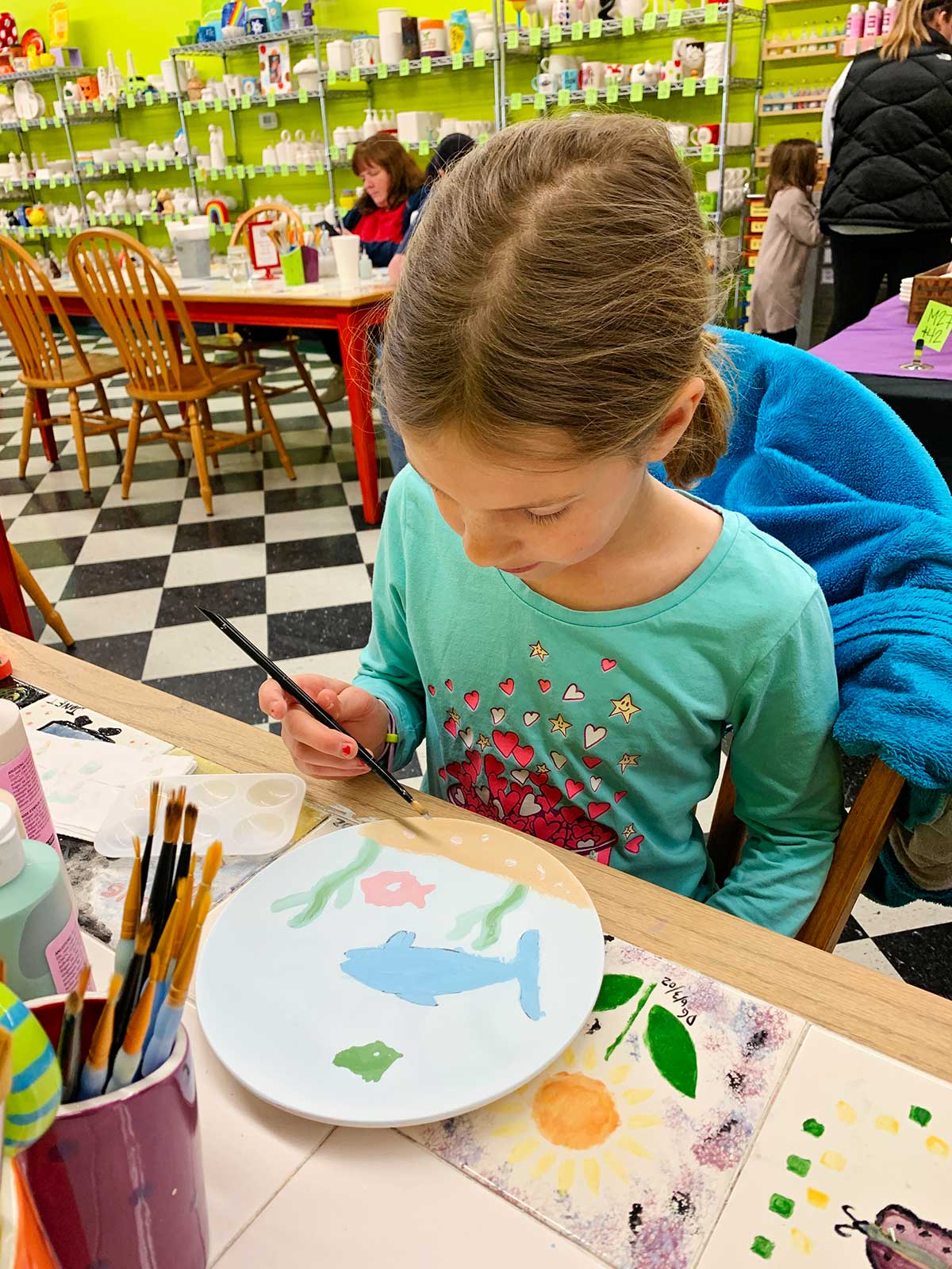Young girl with light brown hair paints her plate at ceramic painting studio.