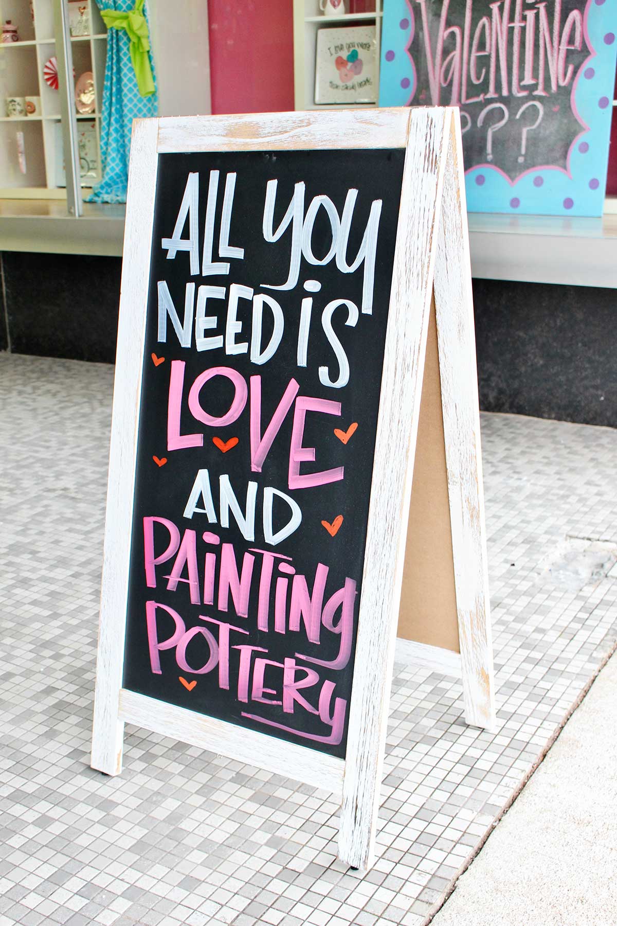 Sign outside of ceramic painting studio that says "All you need is love and painting pottery"