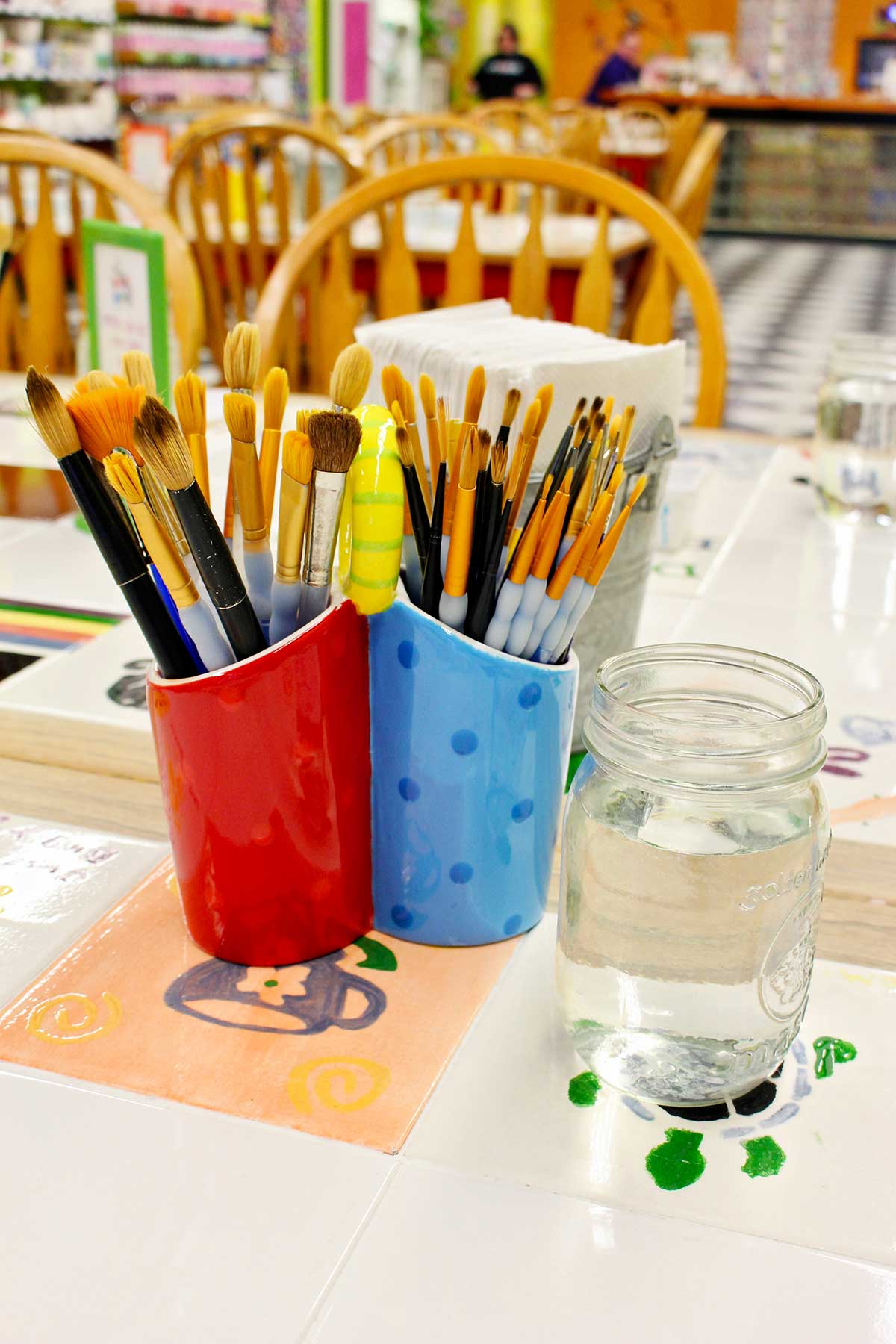 Cups of brushes and a jar of water on a table at the ceramic painting studio.