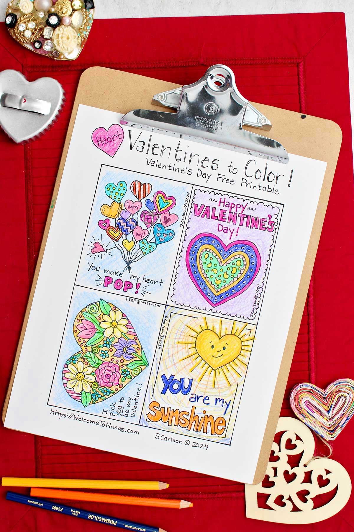 Valentine's Day printable fully colored on clipboard resting on a red placemat with heart shaped objects near by.