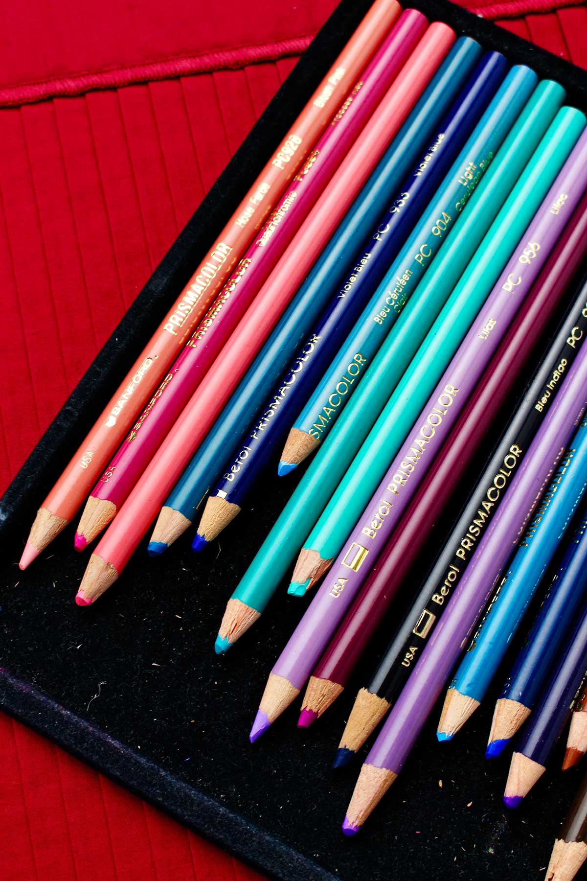 Image of jewel toned colored pencils in case resting on a red placemat.