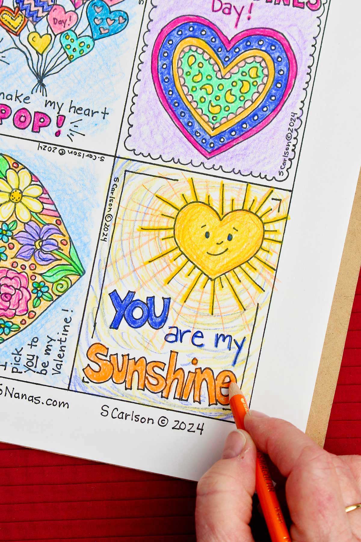 Hand using orange color pencil to shade in the word "sunshine" on Valentine of a heart shaped sun saying "You are my sunshine".