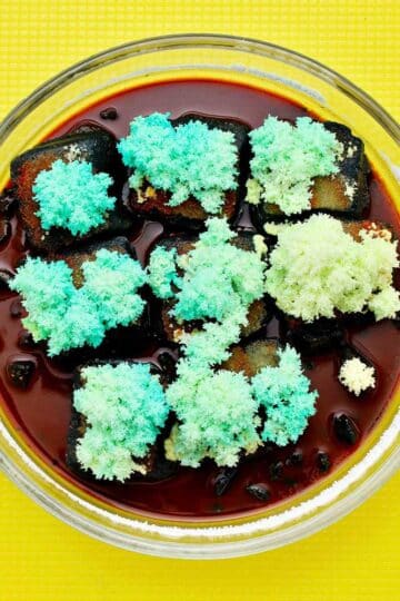 Tray of teal colored crystals on a yellow plastic cutting board.