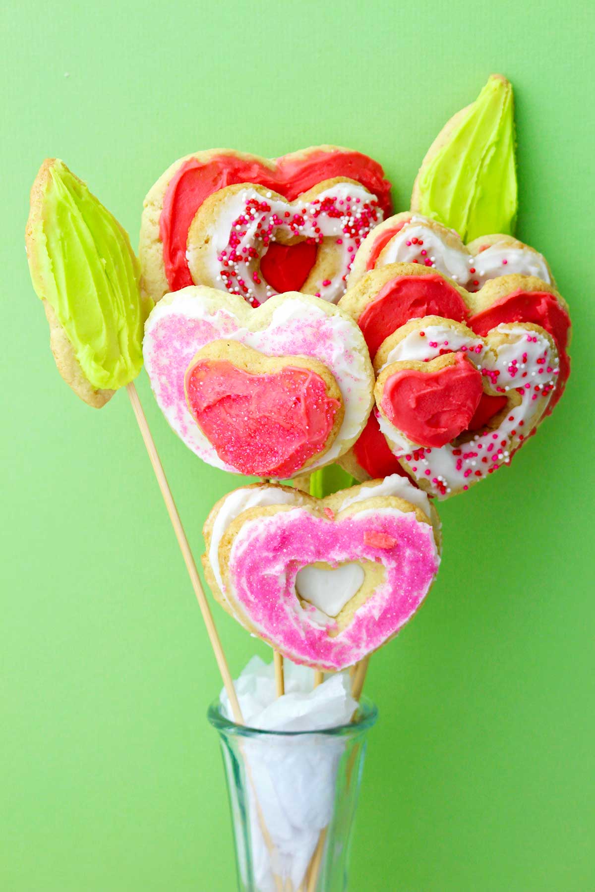 Close up image of a completed sugar cookie bouquet in a vase against a green backdrop.