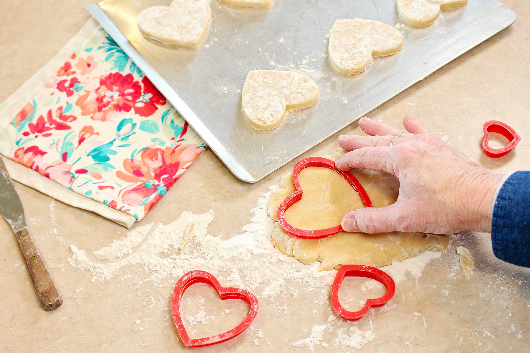 Hand pressing a large red cookie cutter into sugar cookie dough.