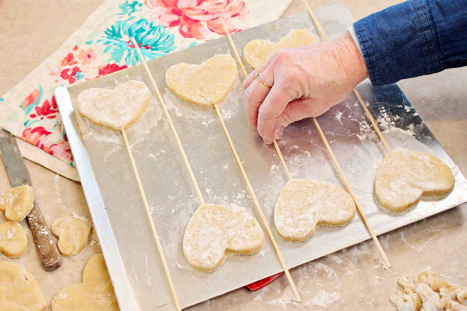 Hand placing wooden sticks into heart shaped dough cutouts.