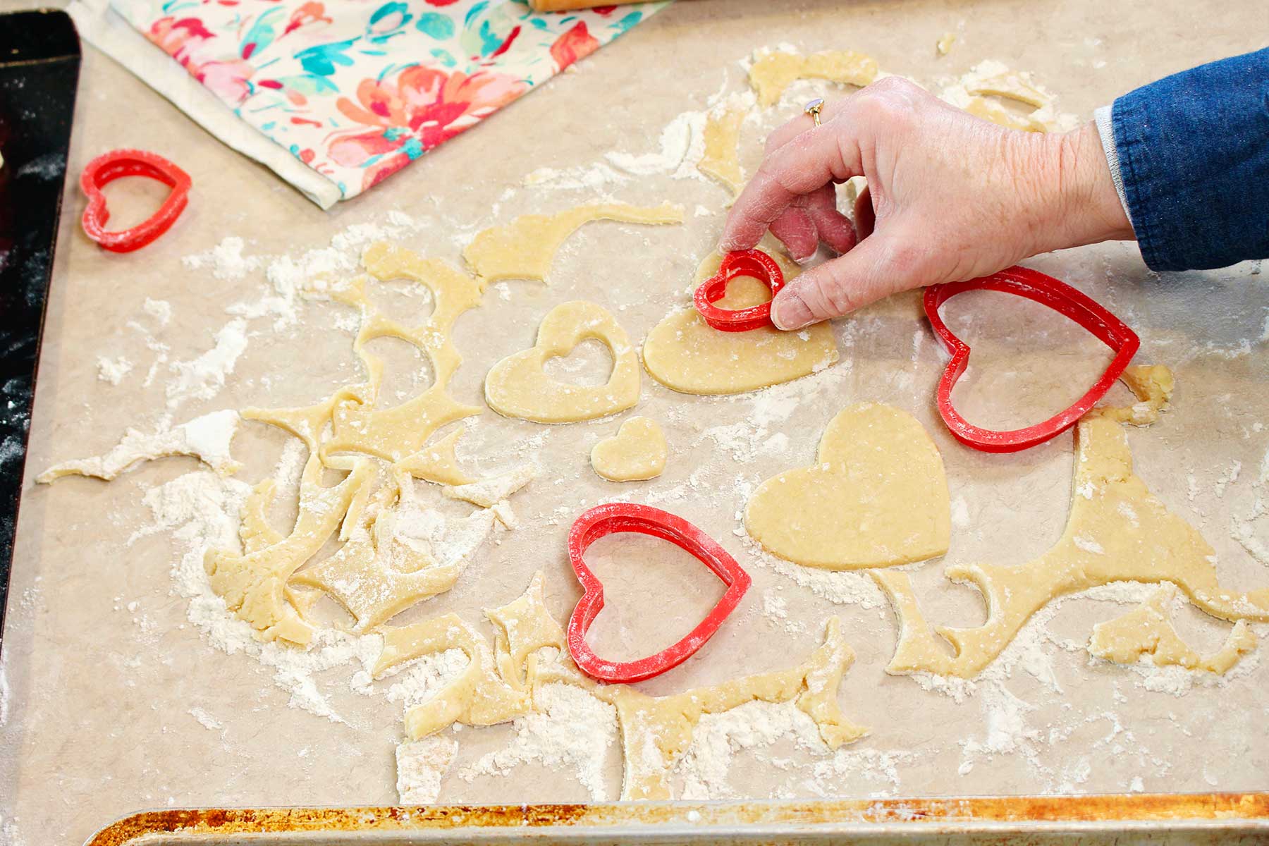 Hand pressing red heart shaped cookie cutter into dough.