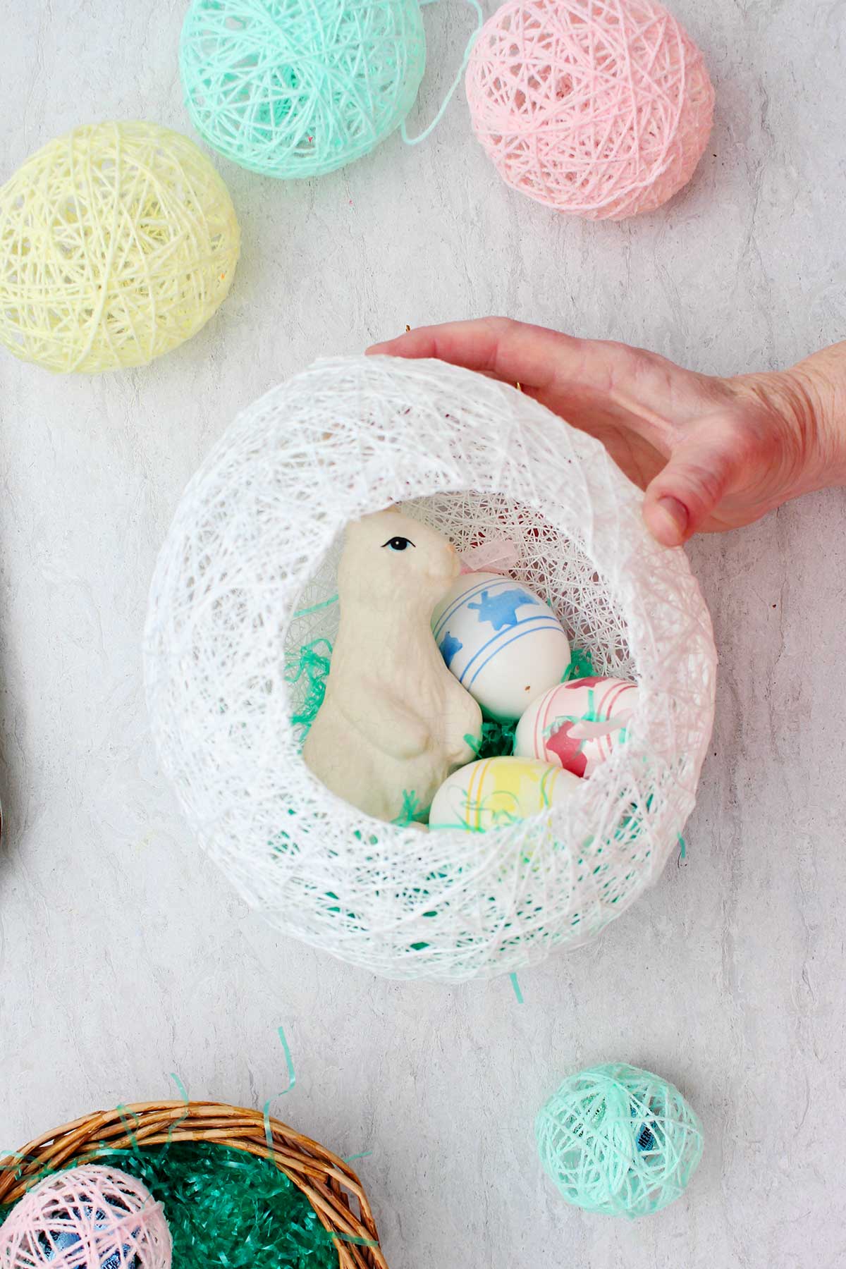 Hand holding white string egg with bunny and Easter eggs inside with other string eggs around it.