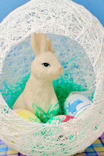 White string egg with hole cut in the side with a white bunny and easter eggs inside.