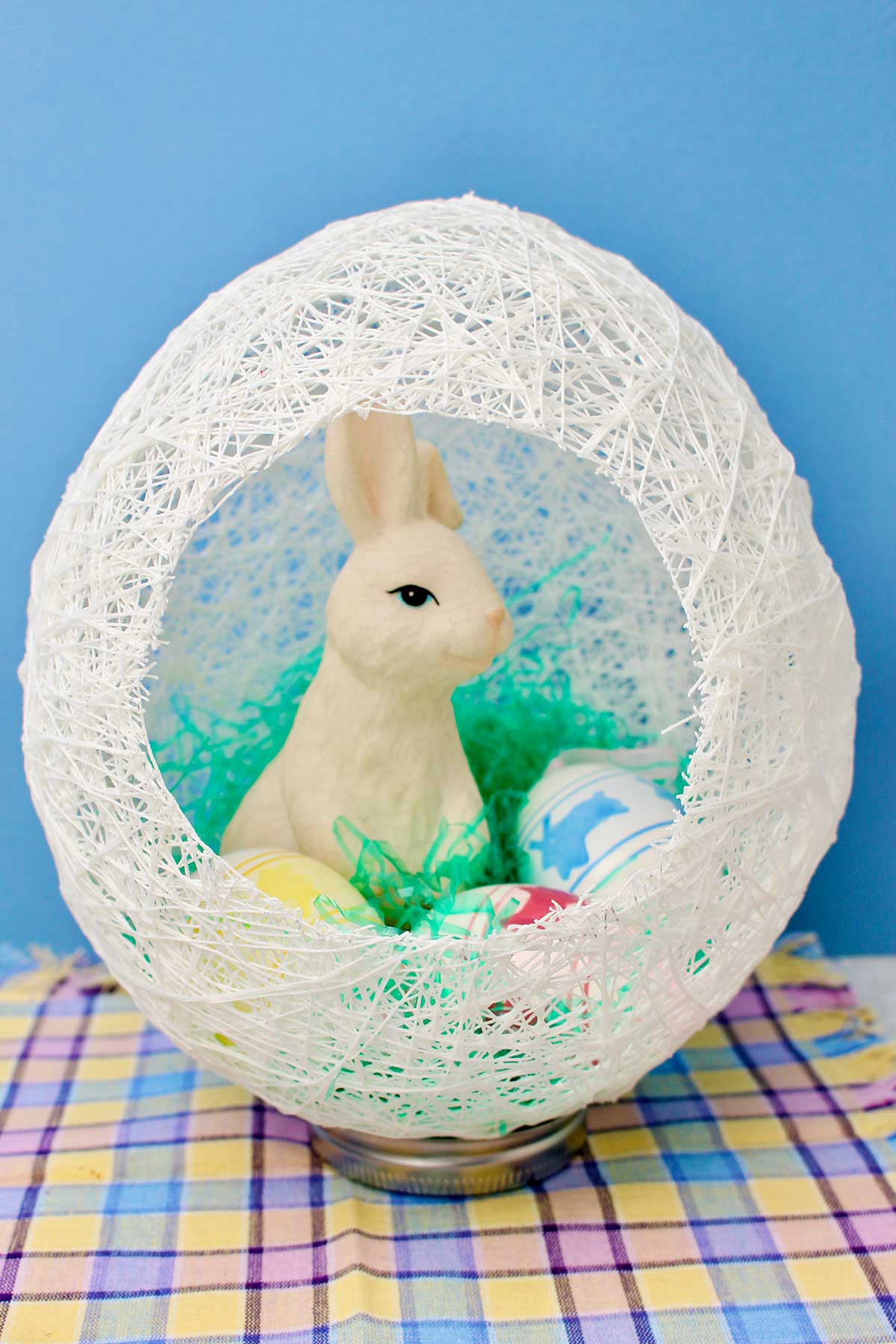 White string egg with hole cut in the side with a white bunny and easter eggs inside.