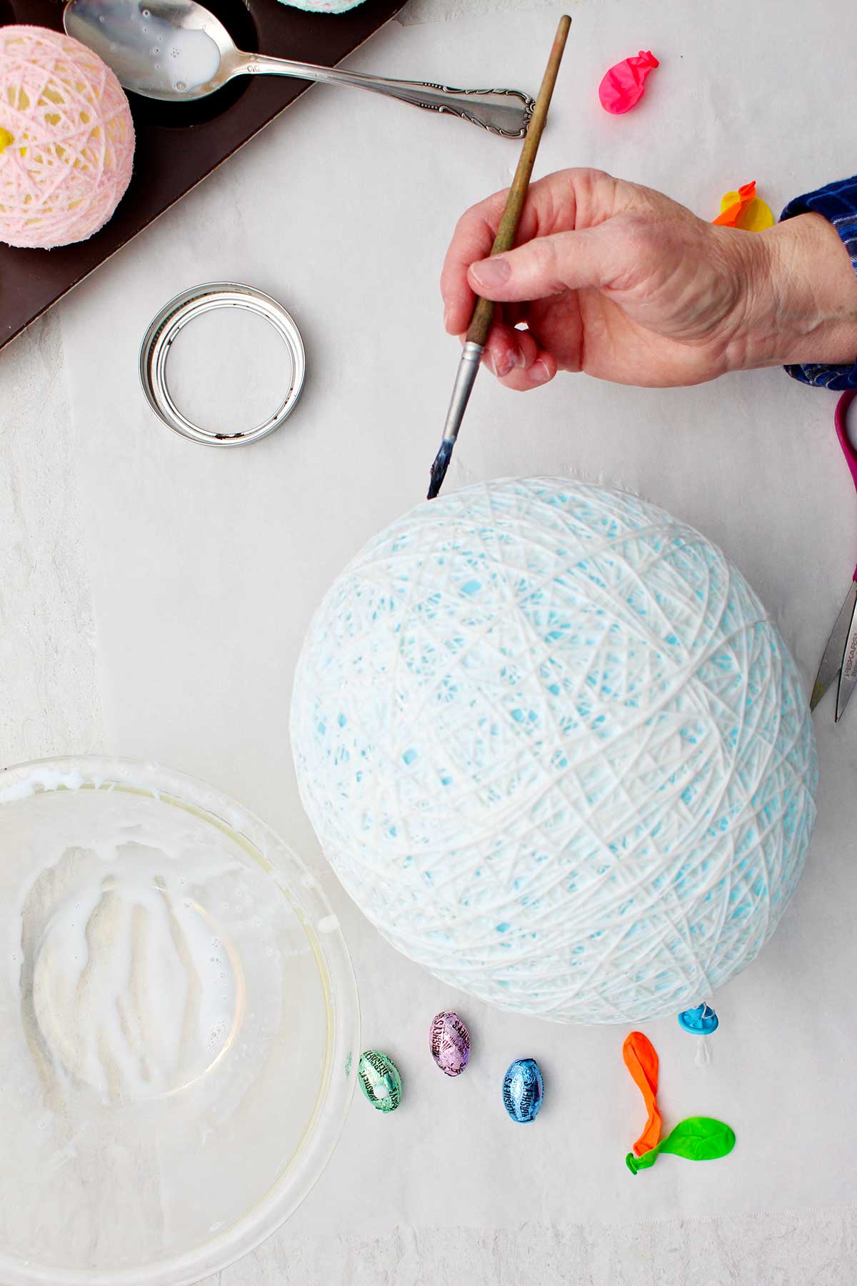 Hand painting white glue on string egg around blue balloon.