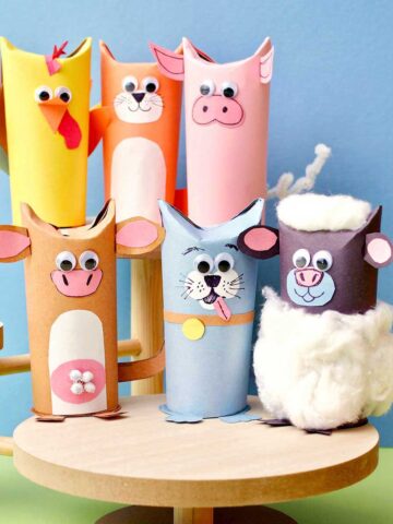 Six cute toilet paper roll animals on wooden stands in front of blue backdrop.