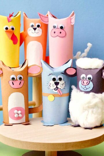 Six cute toilet paper roll animals on wooden stands in front of blue backdrop.